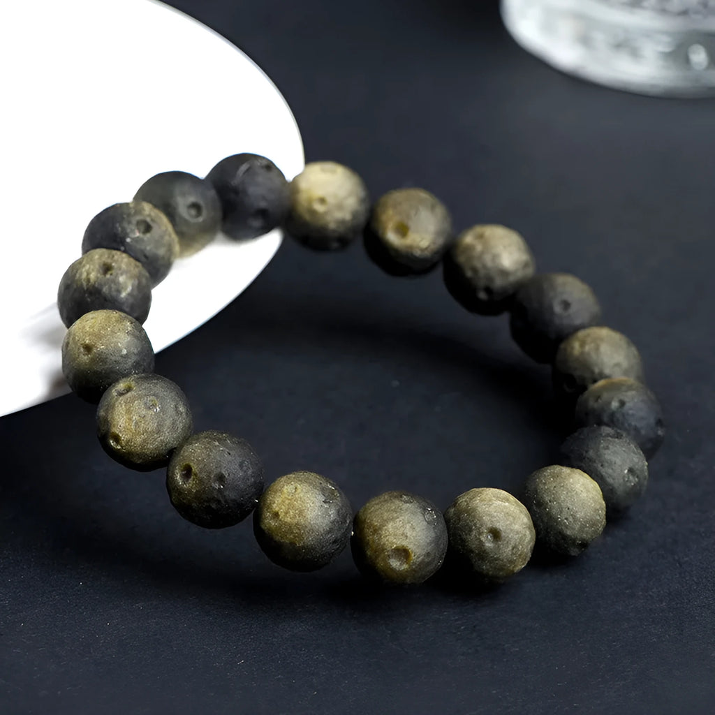 Close-up of an obsidian crater ball bead bracelet showing textured surface from grinding treatment, in silver stone meteorite finish.
