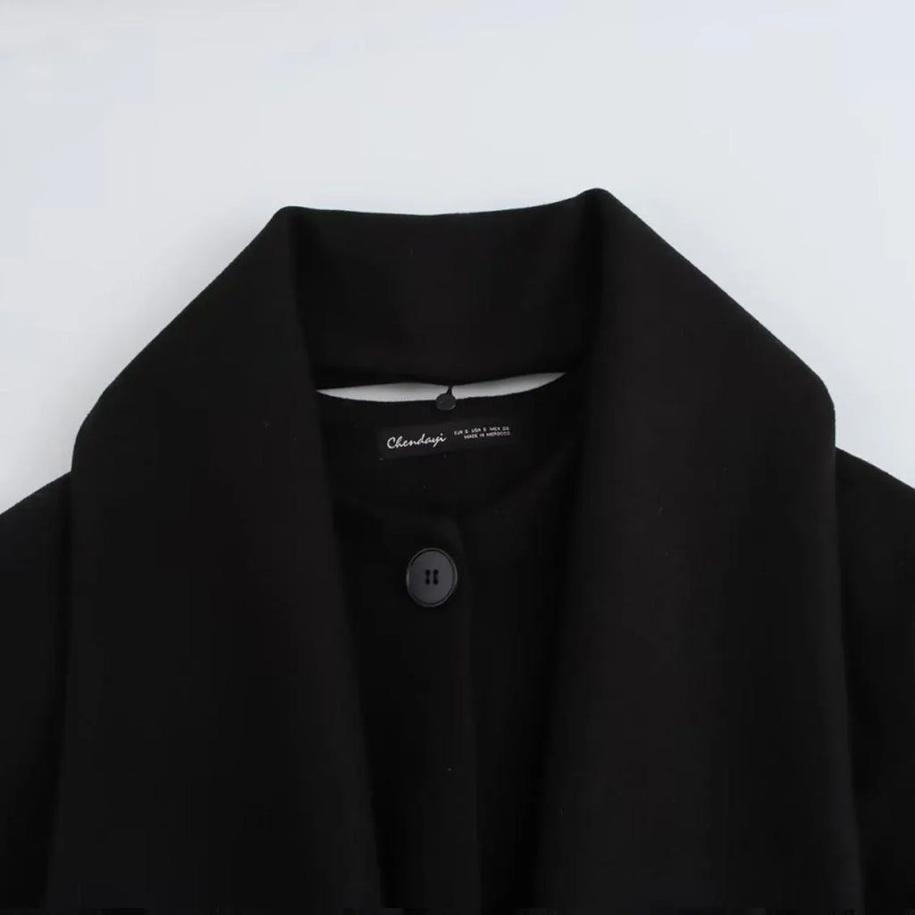 Women's long black coat with a detachable grey artificial fur collar, showing longline silhouette and side pockets.