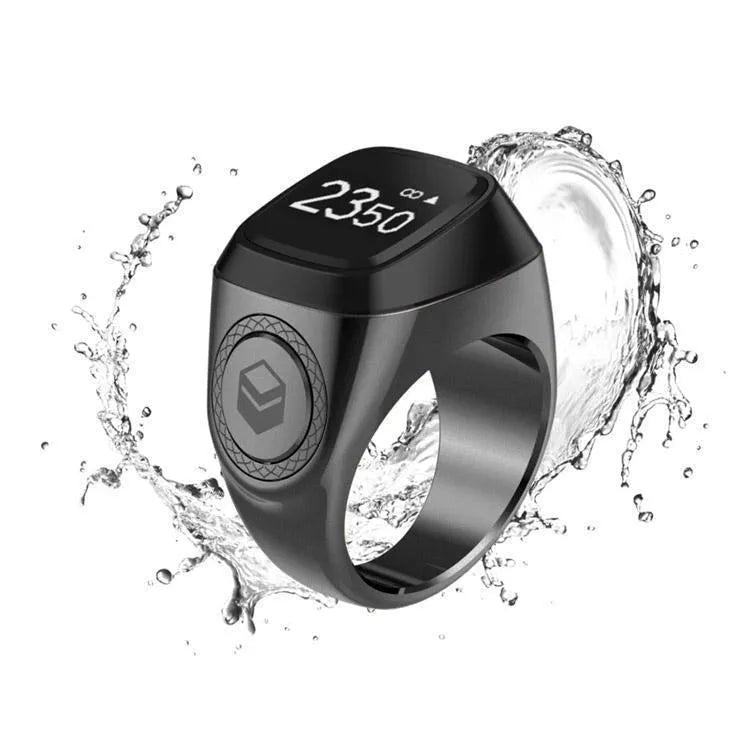 Silver smart ring with a small OLED display showing prayer count, next to its USB charging case.