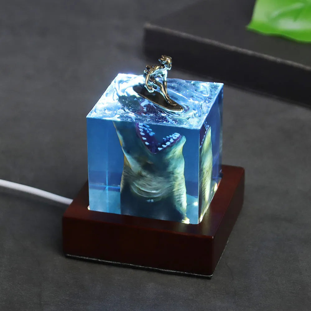Clear epoxy resin ornament with a shark surfing scene inside, shown next to a 5cm and 8cm size option.