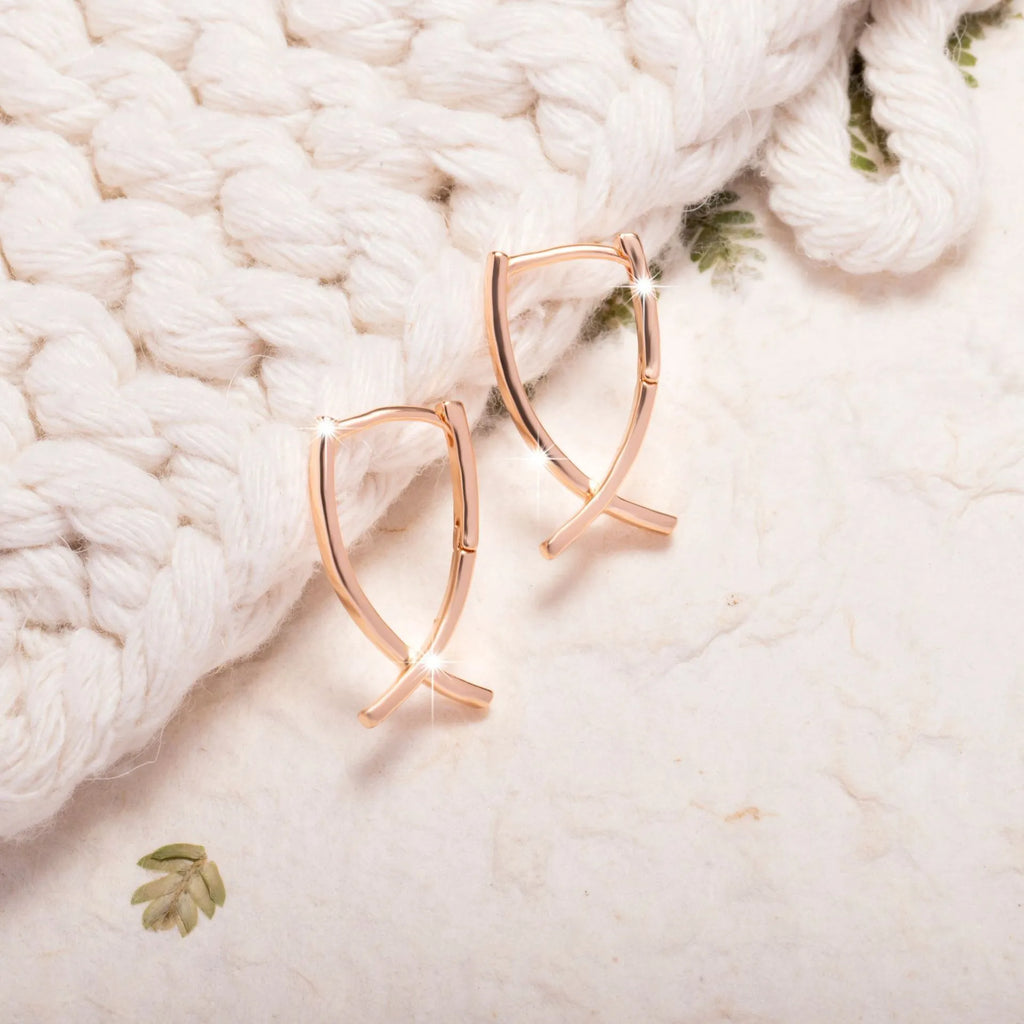 A pair of rose gold coloured cross shaped earrings made from copper on a white background.