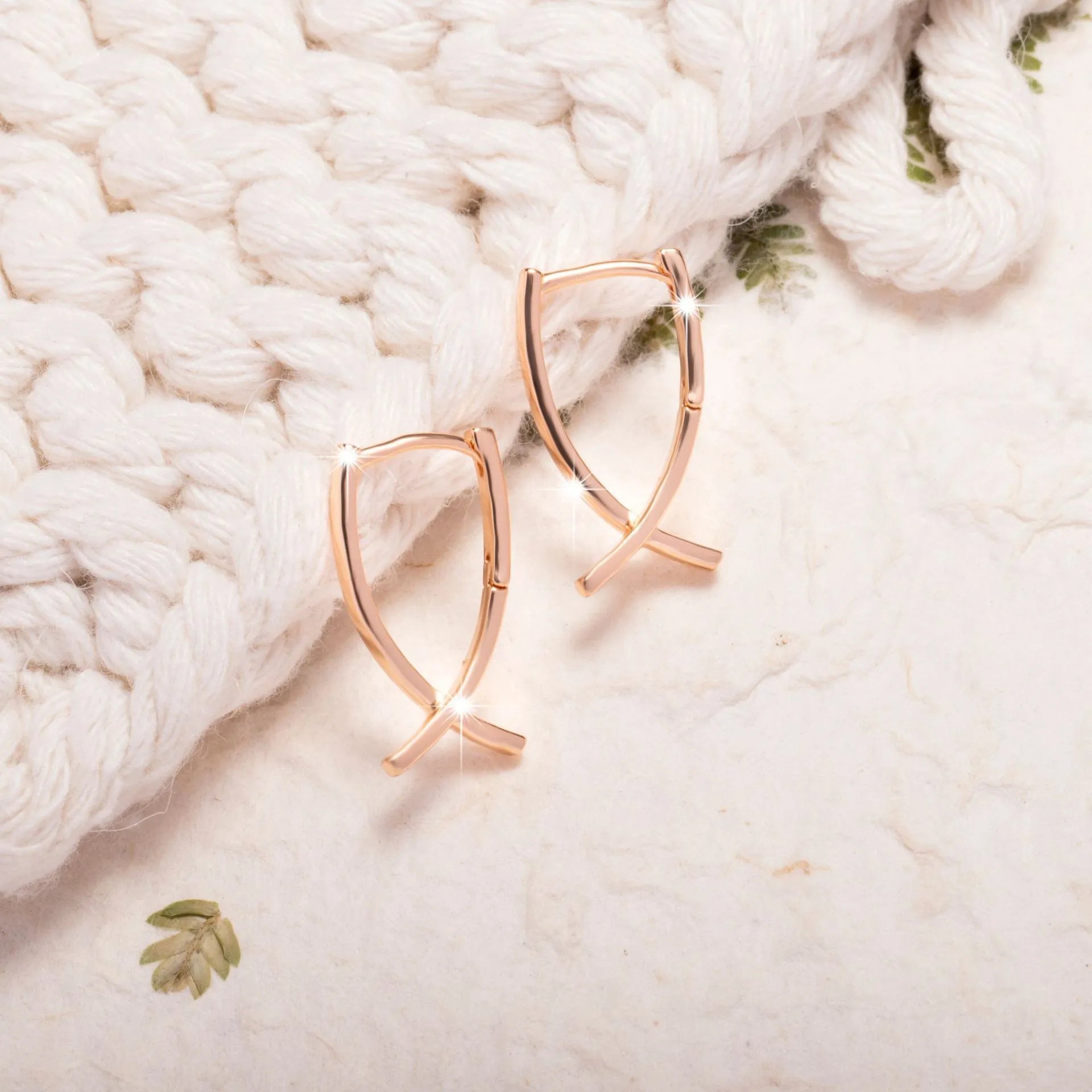 A pair of rose gold coloured cross shaped earrings made from copper on a white background.