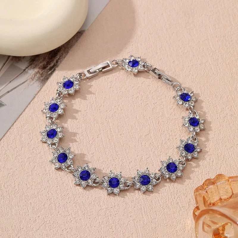 Gold tone flower-shaped bracelet with blue crystal gems on a wrist.