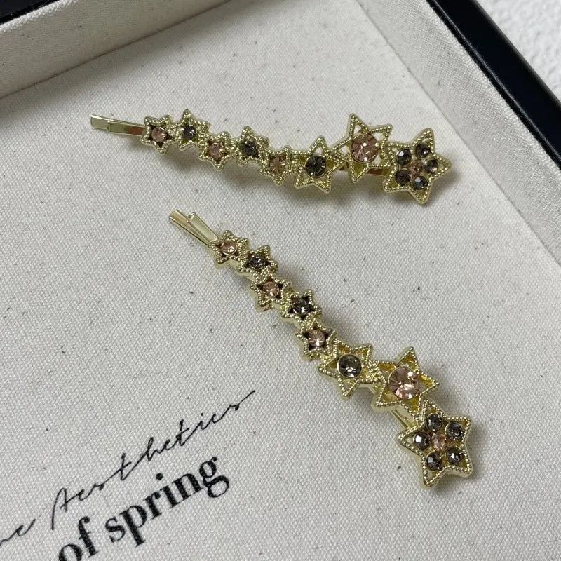 Gold-coloured alloy hair barrette with rhinestone star charm, shown clipped to hair.