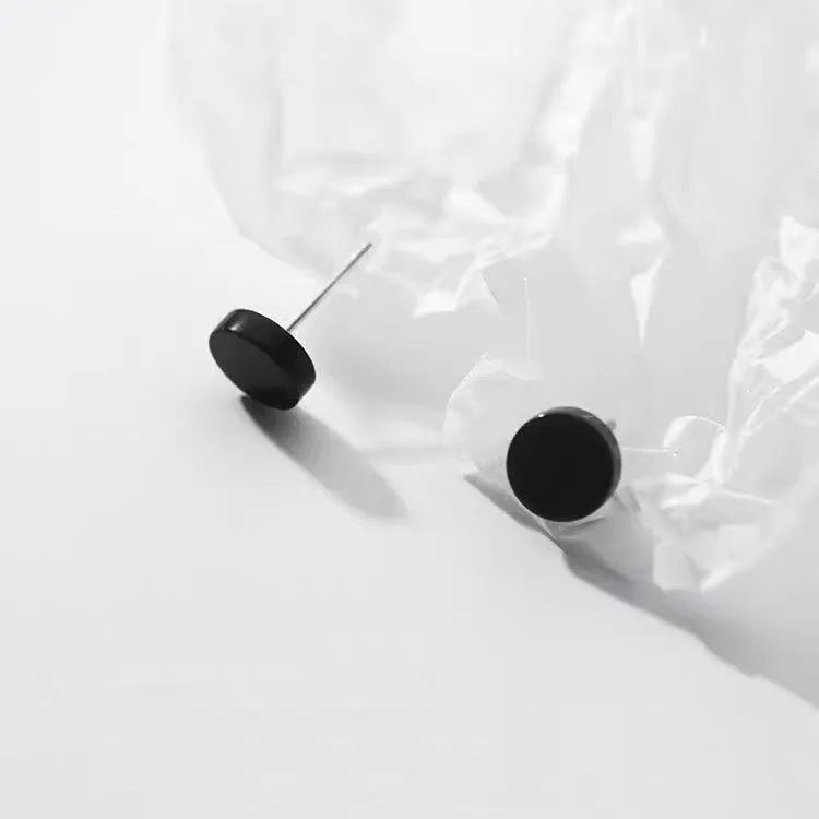 A pair of simple round sterling silver S999 stud earrings on a flat surface, shown in silver and black finishes.