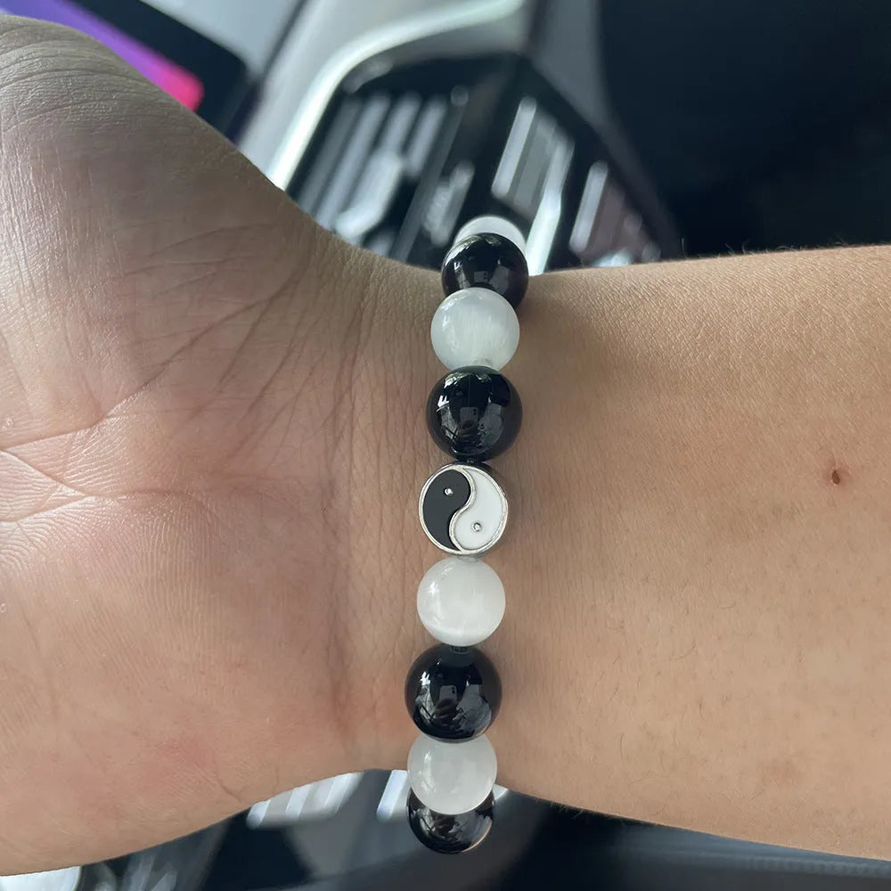 Close-up of a polished opal agate Tai Chi bracelet with a black agate yin-yang symbol on a wrist.
