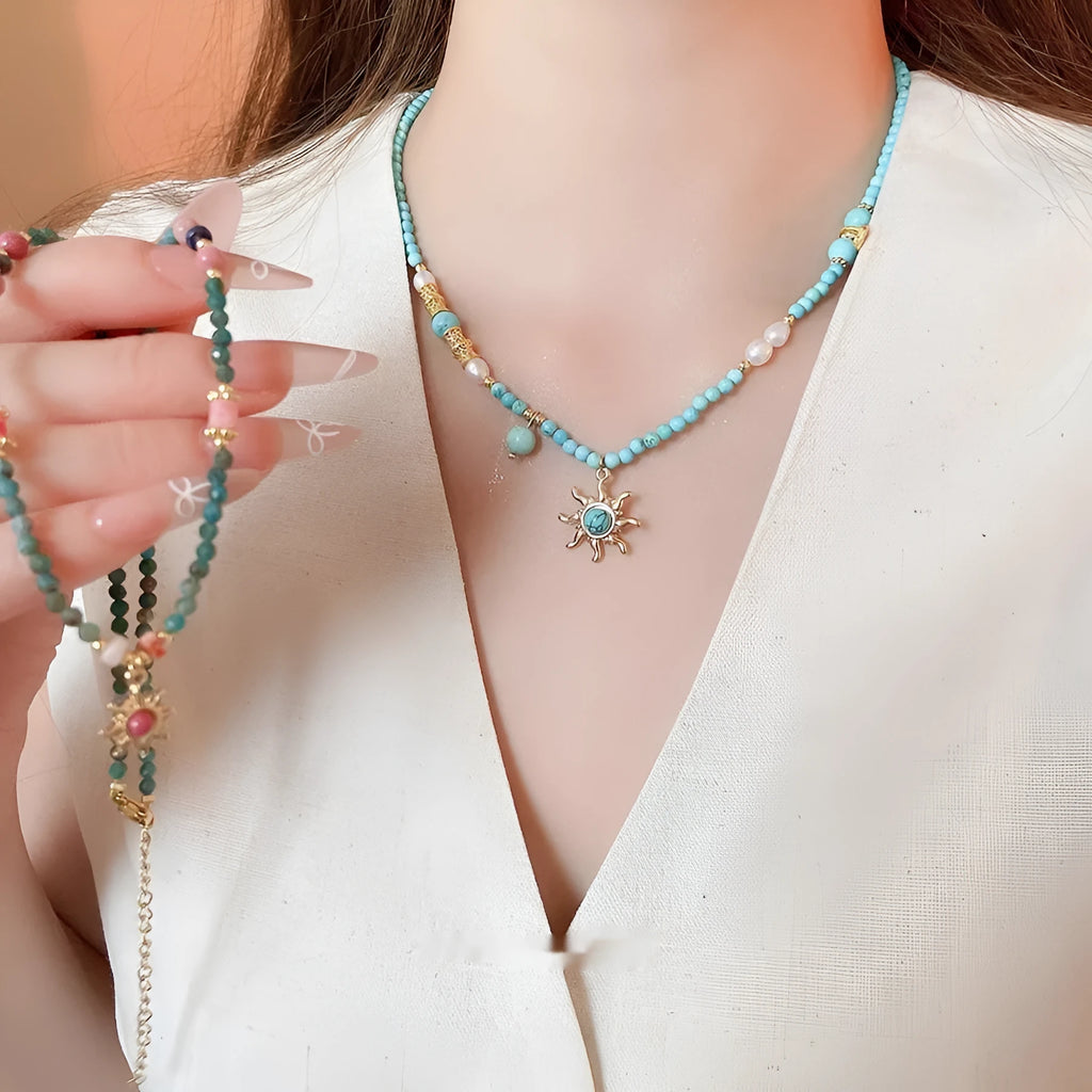 Freshwater pearl necklace with a geometric stone sun pendant on a gold, blue, and pink chain.