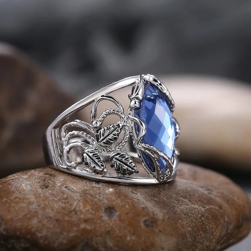 Women's horse eye shaped blue crystal alloy ring on a finger, showing geometric design.