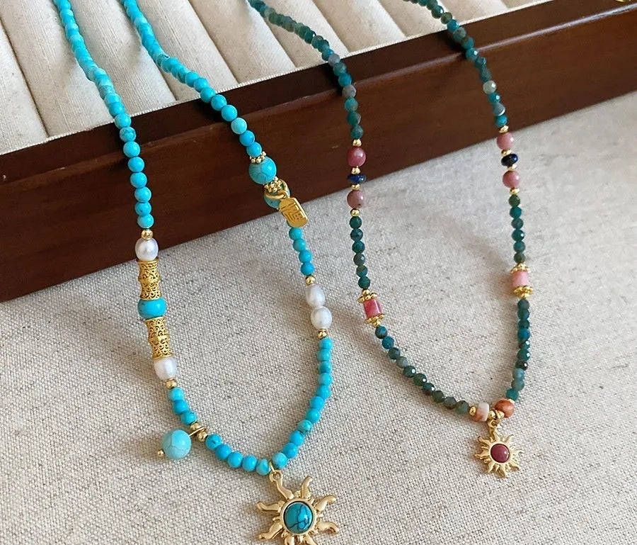 Freshwater pearl necklace with a geometric stone sun pendant on a gold, blue, and pink chain.