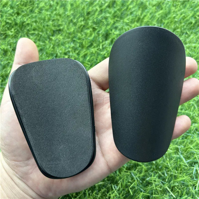 Extra small black and white plastic football shin guards for junior players, size 8cm by 5cm.