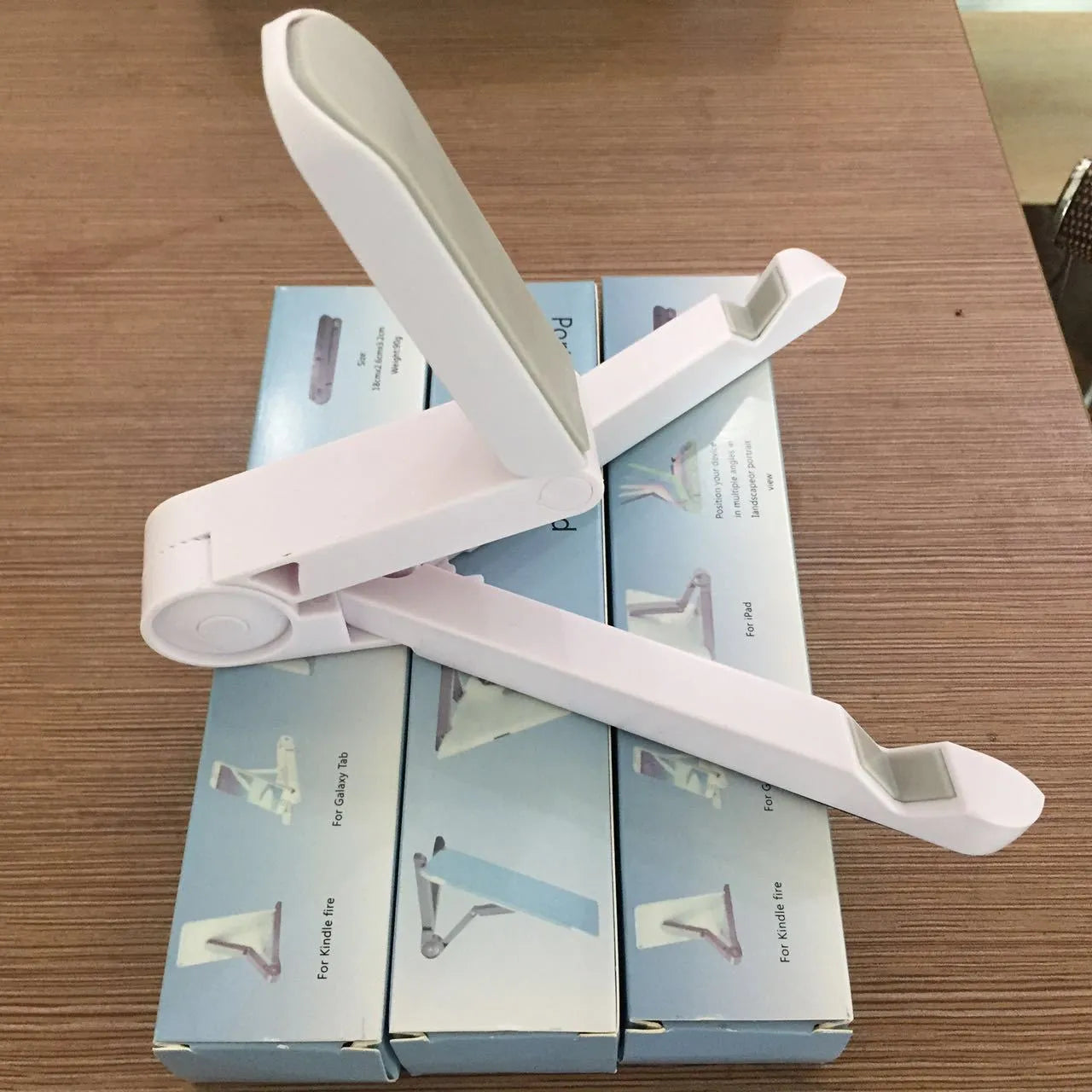 Black foldable tablet holder open in landscape mode holding a smartphone, showing its adjustable angle and non-slip base.