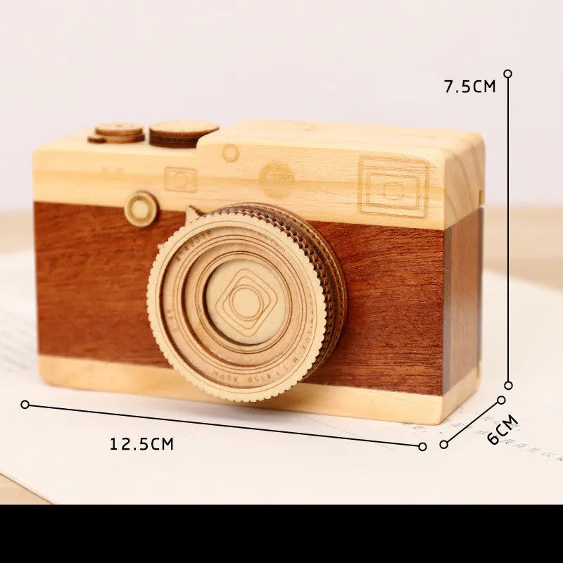 Camera-shaped pine wood music box with rotating sanding box mechanism on a white background.