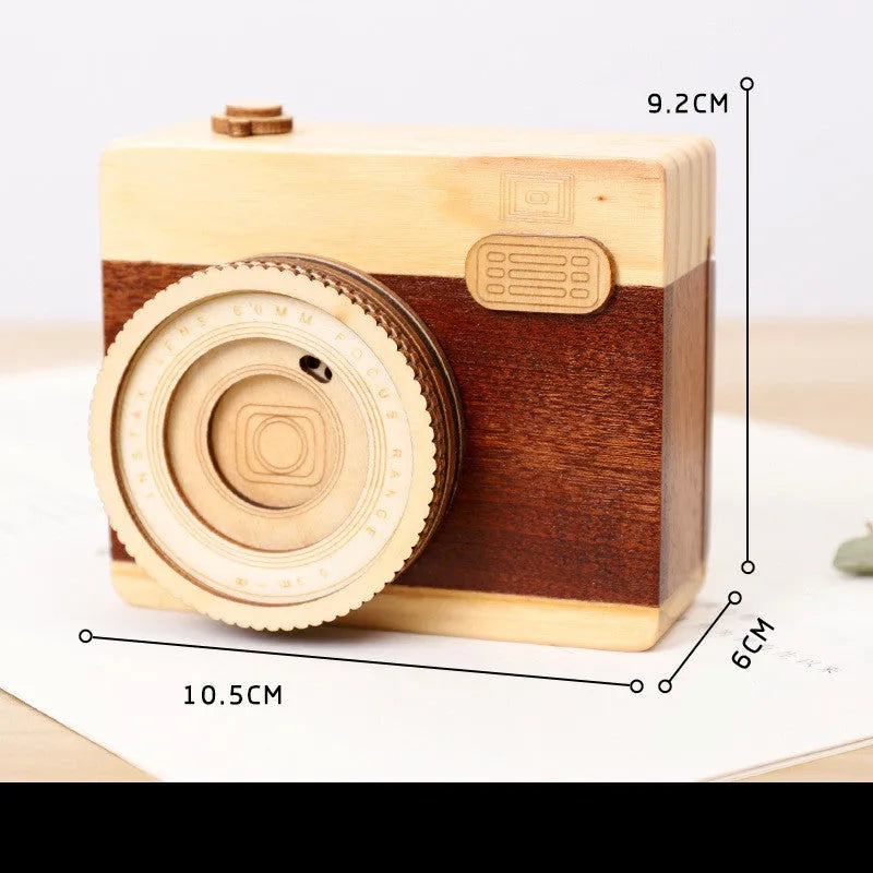 Camera-shaped pine wood music box with rotating sanding box mechanism on a white background.