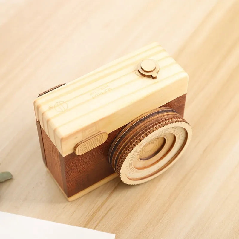 Camera-shaped pine wood music box with rotating sanding box mechanism on a white background.
