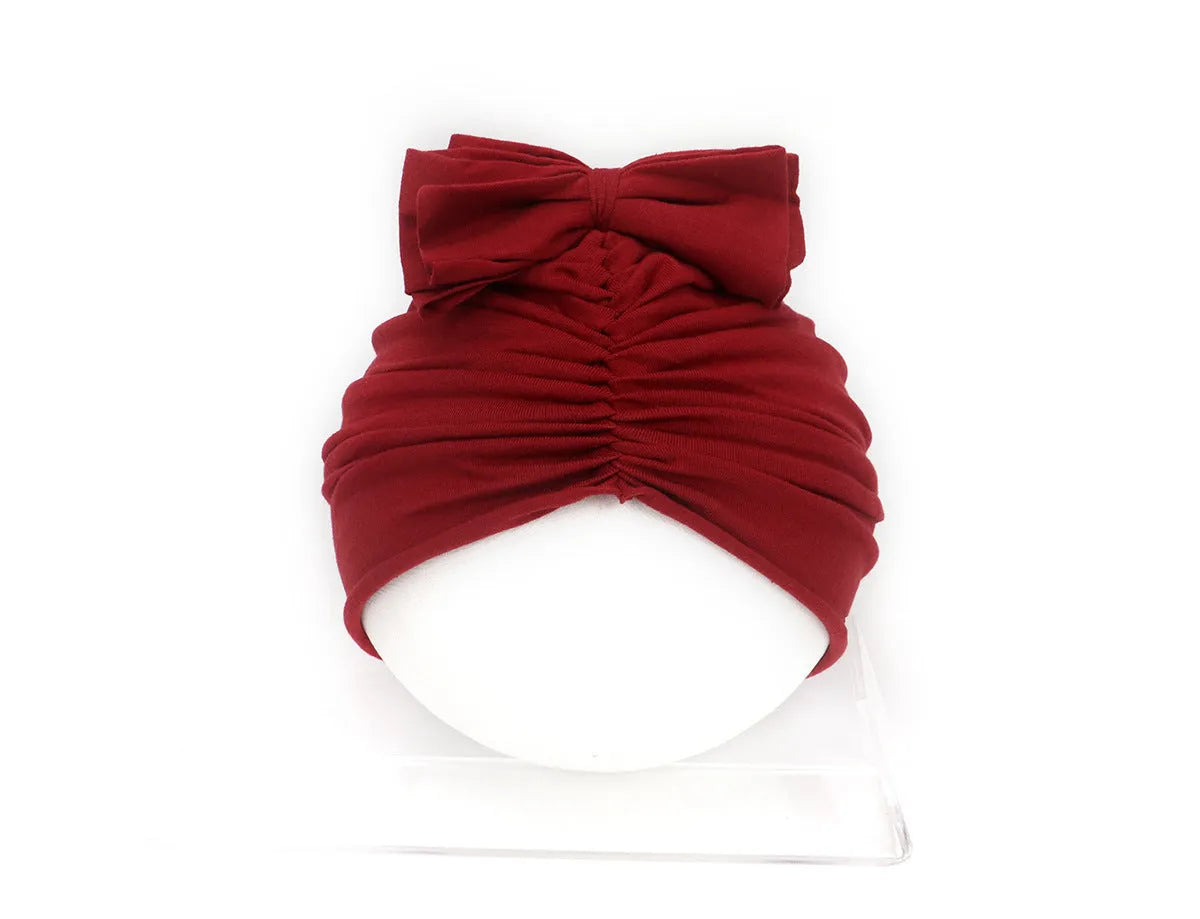 Baby girl wearing a soft pink knitted turban-style cap for ages 0-28 months.
