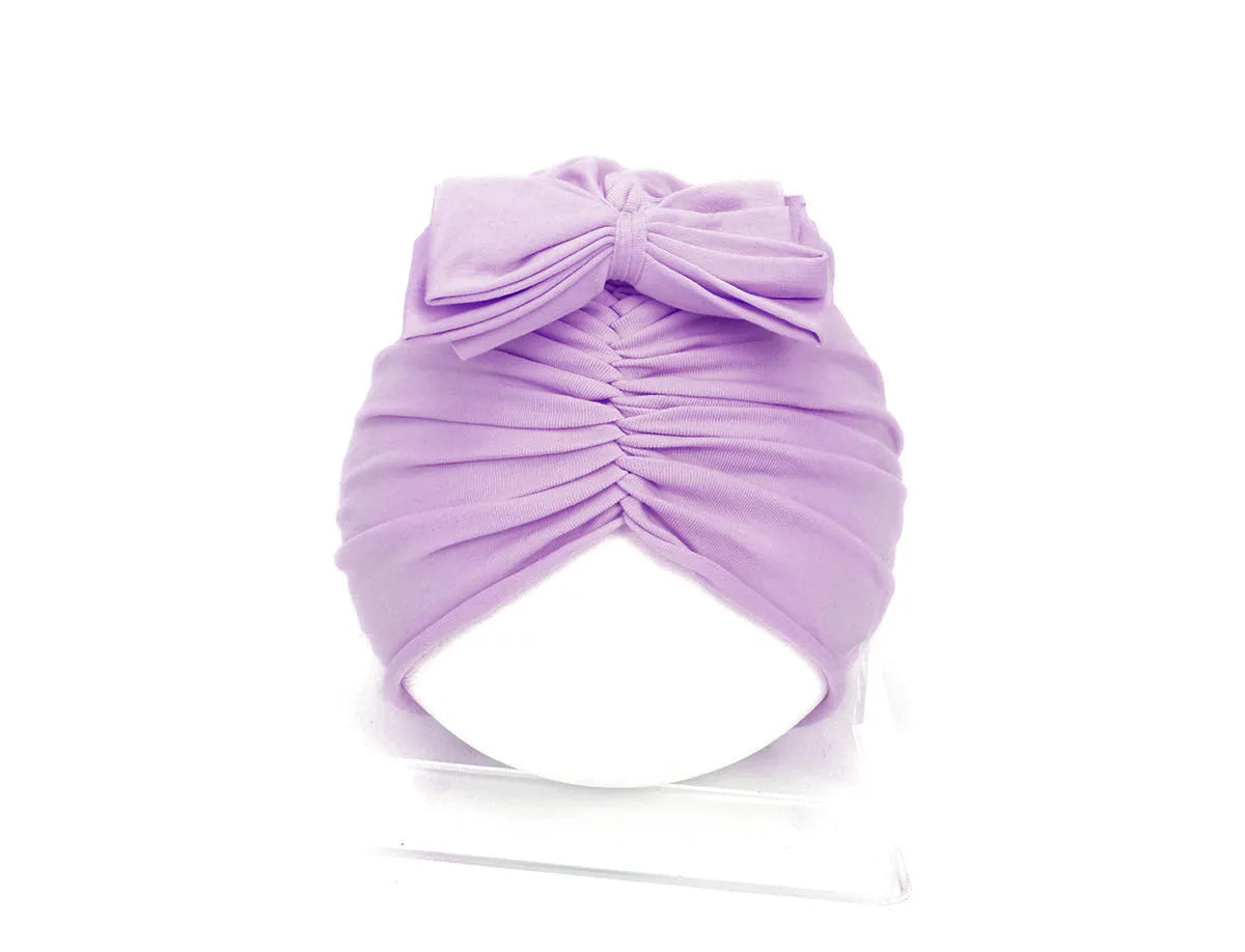 Baby girl wearing a soft pink knitted turban-style cap for ages 0-28 months.
