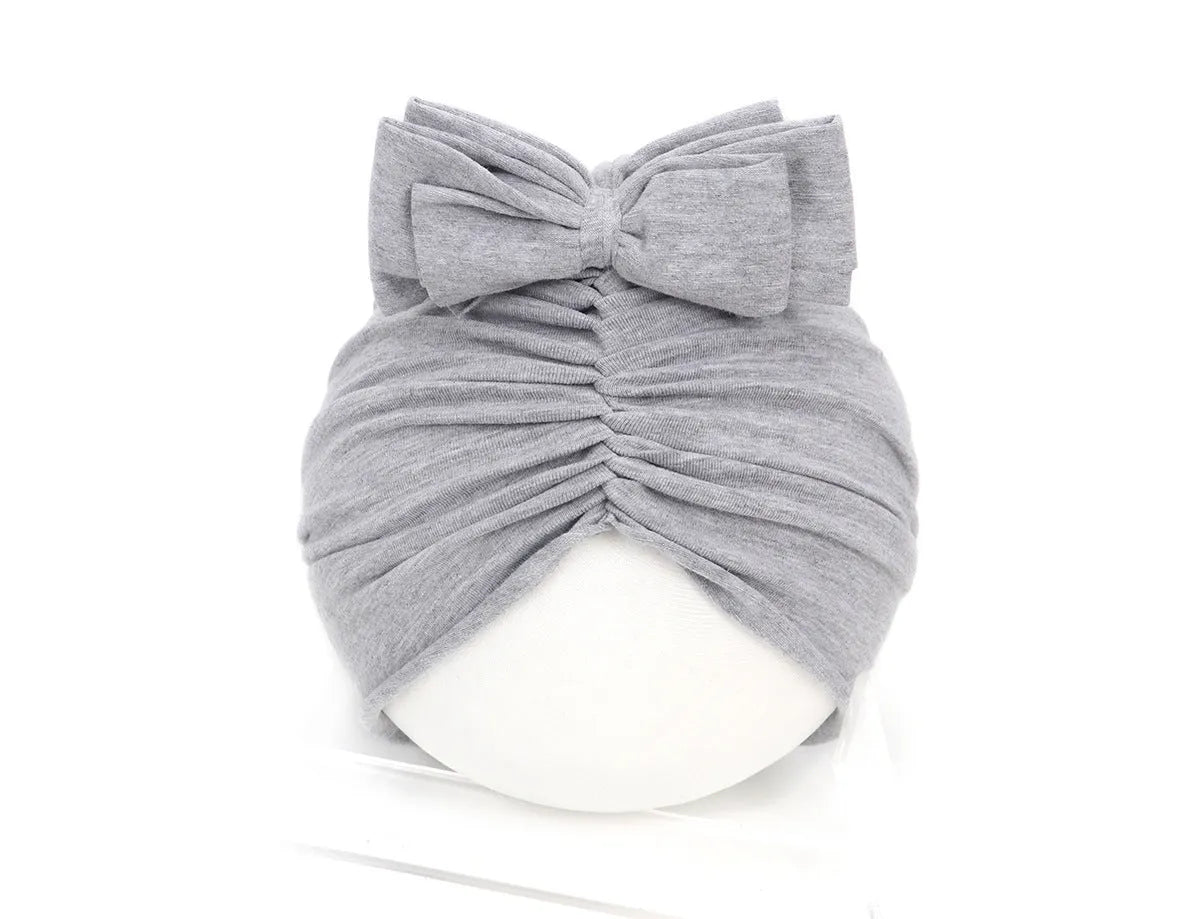 Baby girl wearing a soft pink knitted turban-style cap for ages 0-28 months.