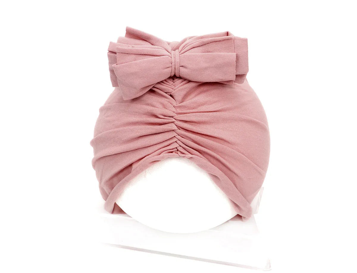 Baby girl wearing a soft pink knitted turban-style cap for ages 0-28 months.