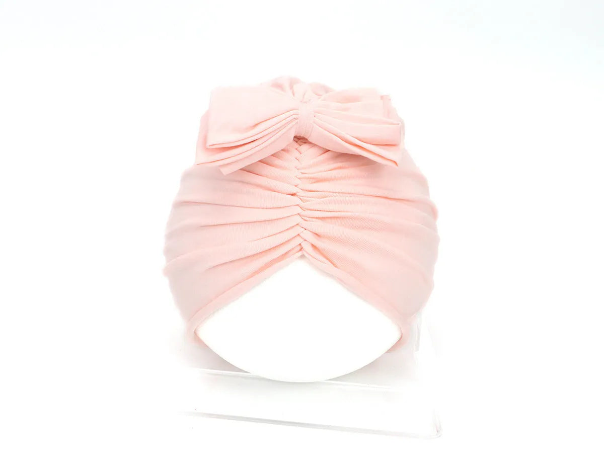 Baby girl wearing a soft pink knitted turban-style cap for ages 0-28 months.