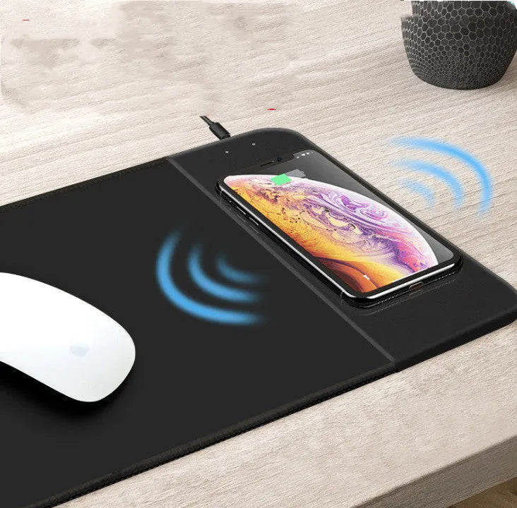 Wireless charging mouse pad with RGB edge lighting and cartoon graphic on black cloth surface.