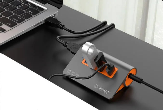 Dark grey aluminium USB hub with four orange-trimmed ports and a long black data cable.