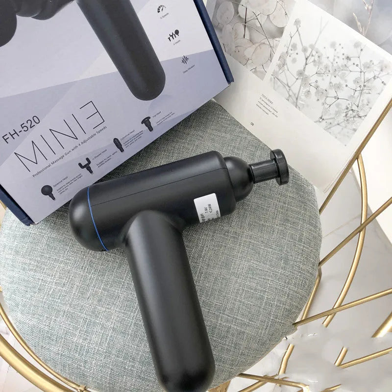 Grey, red, and black handheld fascia gun massager on a table with USB charging cable.