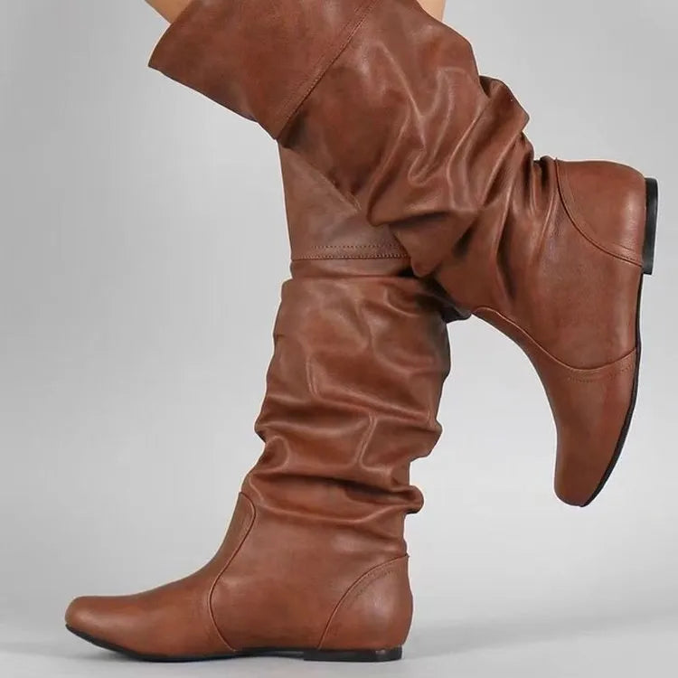 Women's black slip-on flat long boots with a round toe and high shaft on a neutral background.