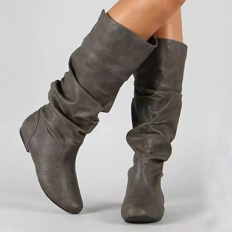 Women's black slip-on flat long boots with a round toe and high shaft on a neutral background.