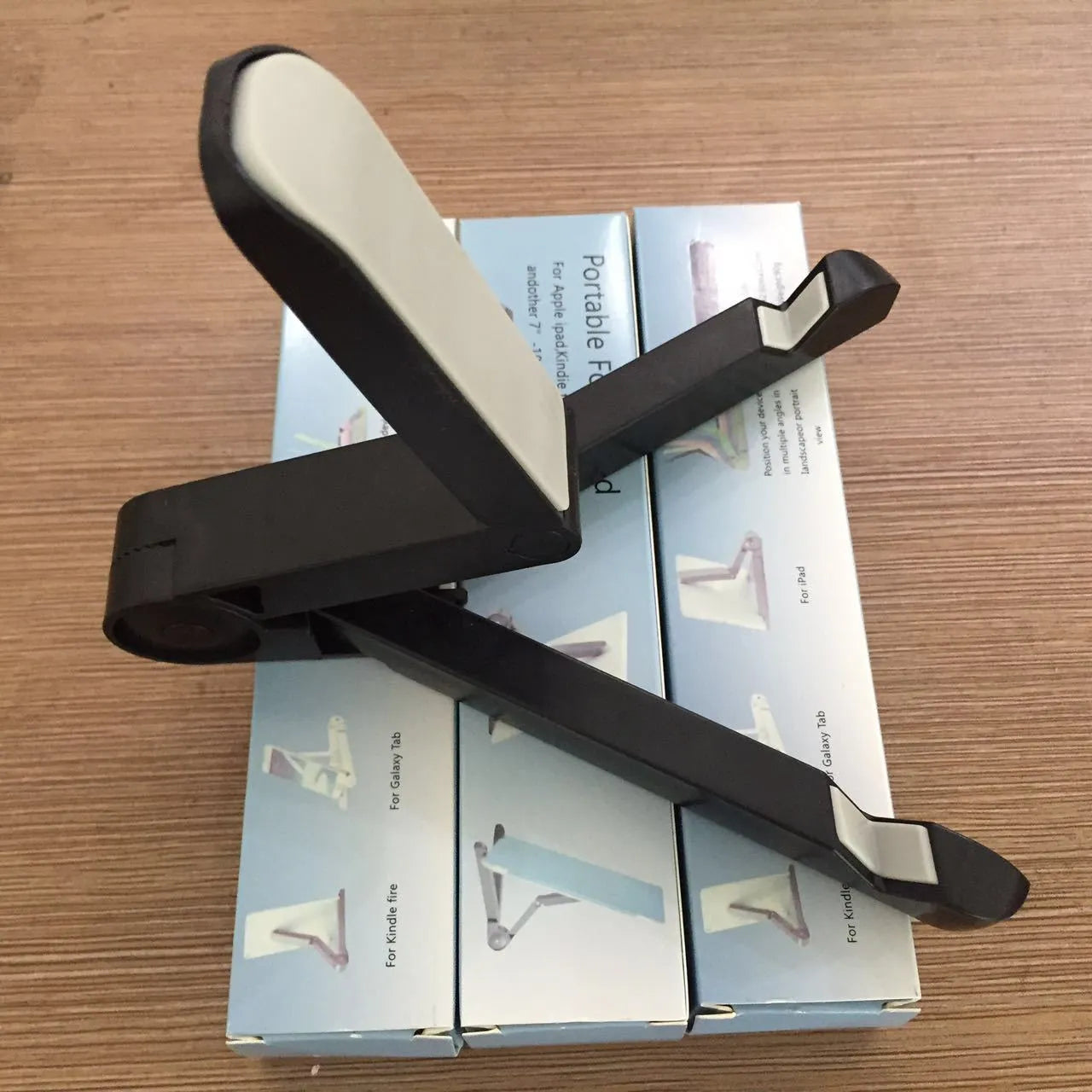 Black foldable tablet holder open in landscape mode holding a smartphone, showing its adjustable angle and non-slip base.
