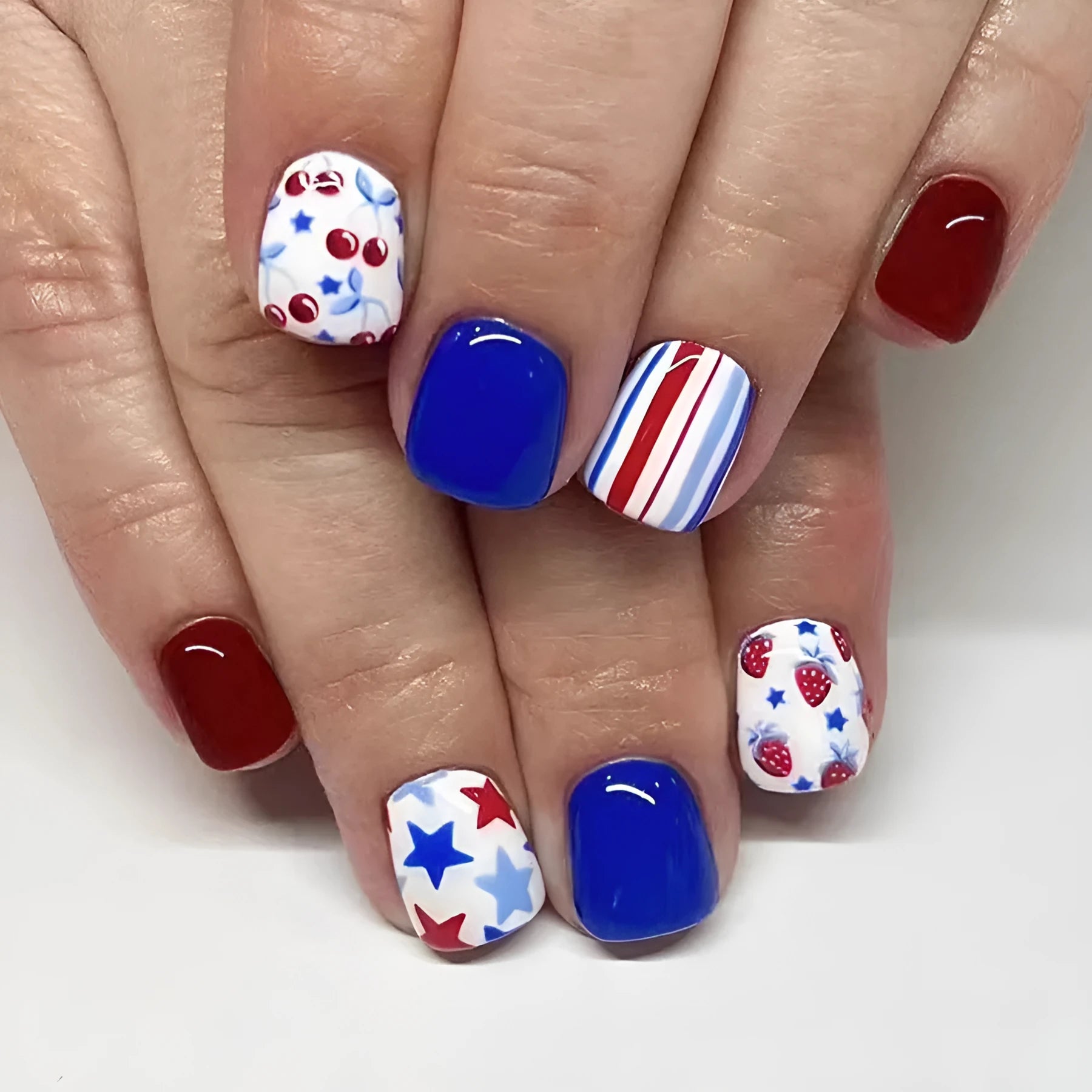 Short glossy false nails with strawberry cherry independence day patterns in red and blue
