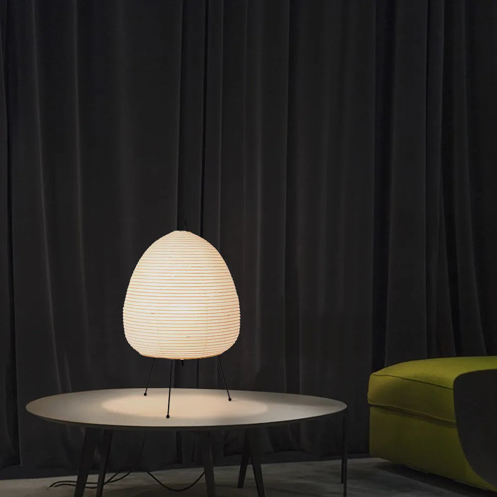 Japanese style table lamp with a white handmade paper lantern shade and aluminium base on a wooden table.