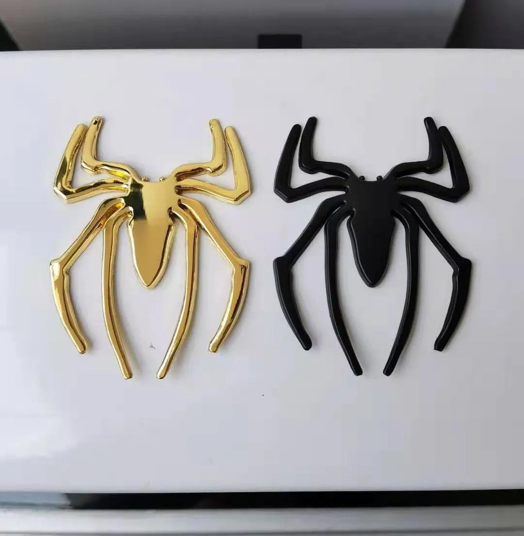 Three-dimensional zinc alloy spider bumper sticker in metallic colours on a surface.