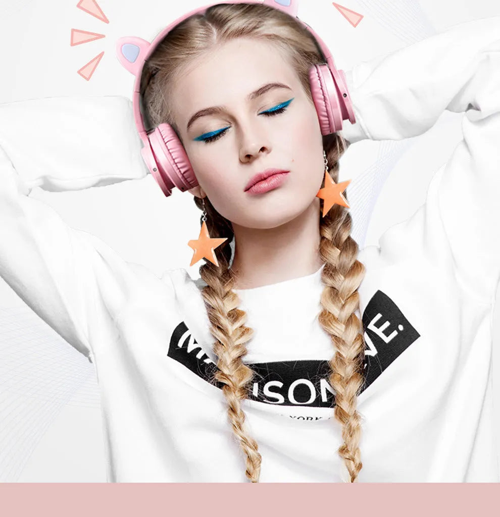 Pink and white wireless Bluetooth over-ear headset with a braided cable on a grey background.