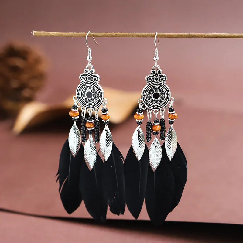 Close-up of a pair of bohemian-style feather-shaped earrings with a leaf pattern, in an alloy electroplated finish.