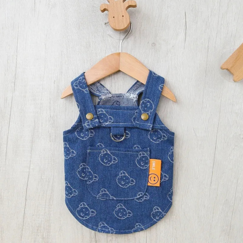 A small dog wearing a light blue denim princess dress with a bracket-style skirt.