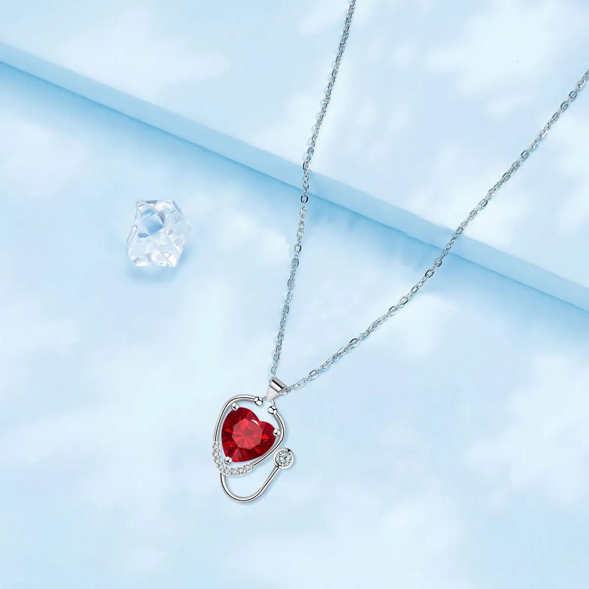 Close-up of a red diamond coloured stethoscope pendant necklace with cross, heart and wing details on a copper chain.