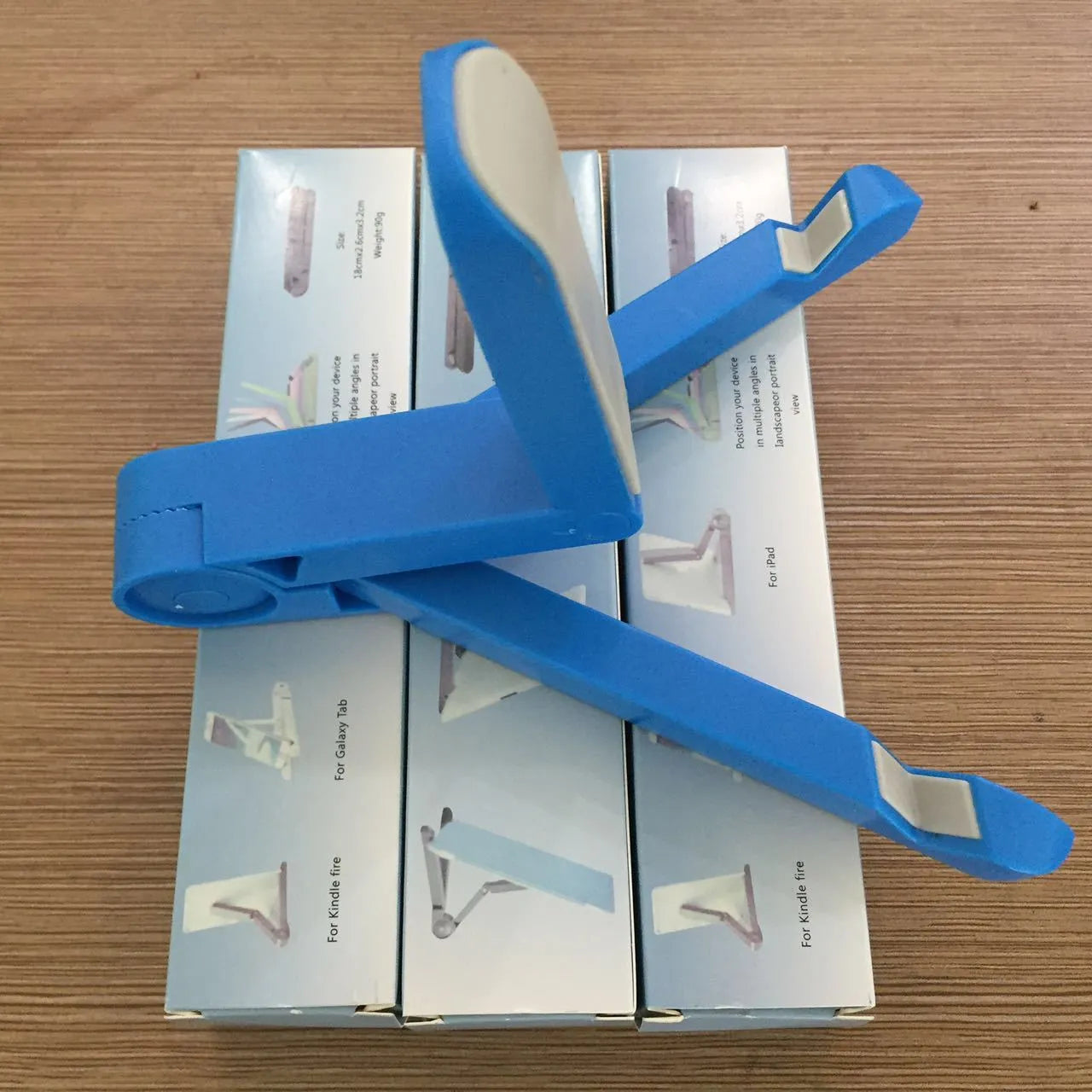 Black foldable tablet holder open in landscape mode holding a smartphone, showing its adjustable angle and non-slip base.