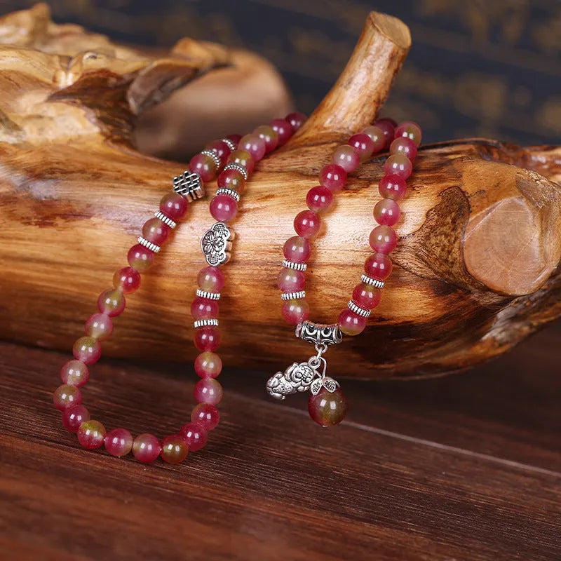 Handmade bracelet with watermelon crystal beads and a red Chinese knot on a white background.