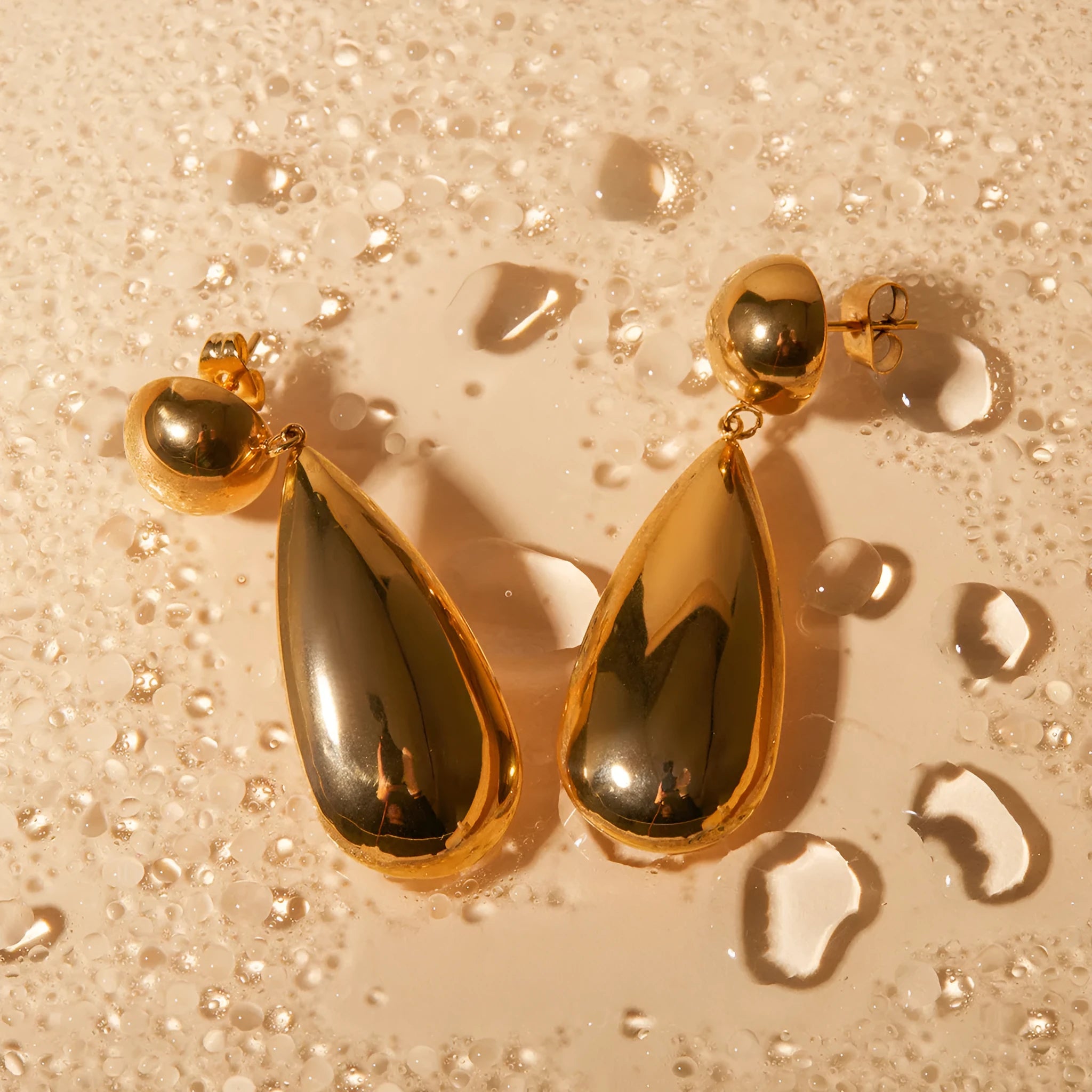 Gold coloured stainless steel earrings with geometric water drop hemisphere pendant design