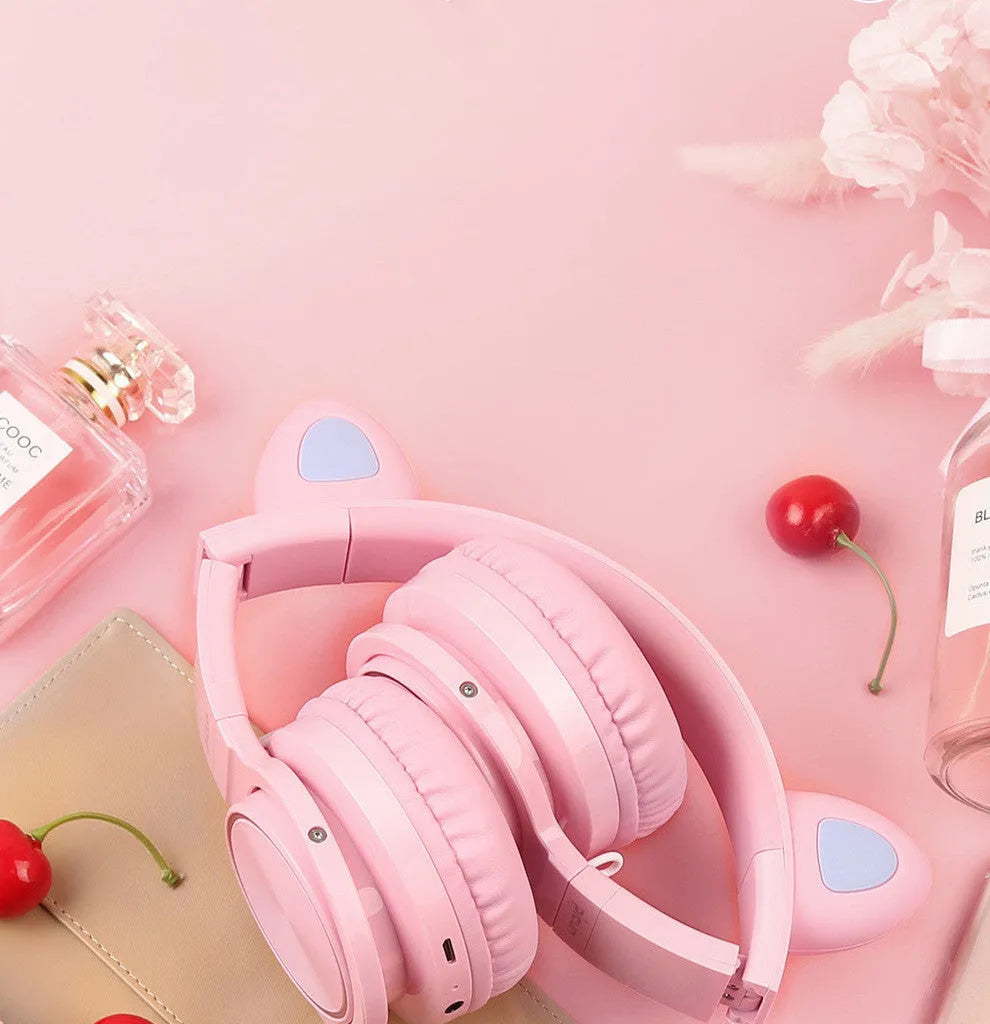 Pink and white wireless Bluetooth over-ear headset with a braided cable on a grey background.