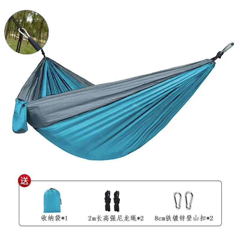 Blue nylon parachute cloth camping hammock hung between two trees outdoors.