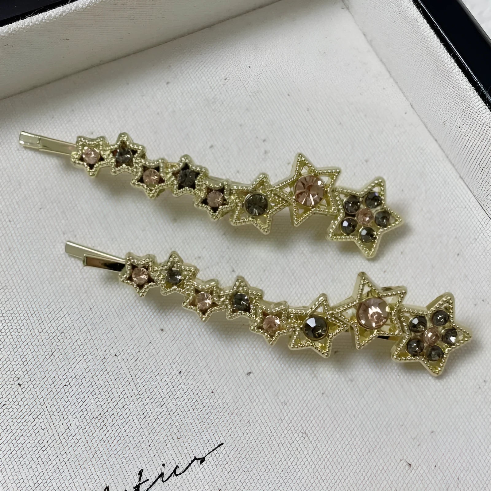Gold-coloured alloy hair barrette with rhinestone star charm, shown clipped to hair.