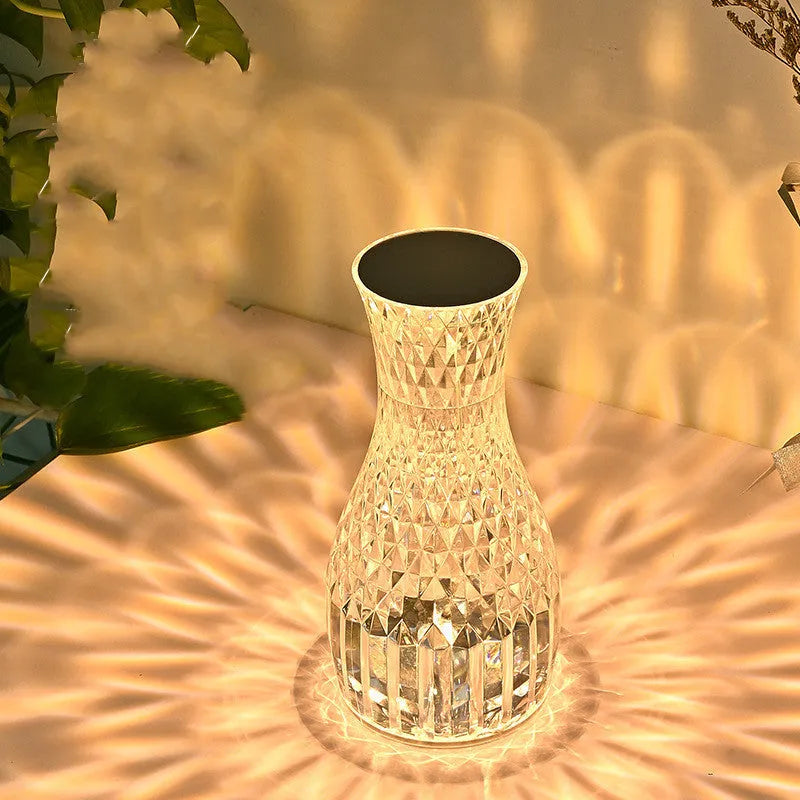 White crystal vase-shaped table lamp with remote control on a wooden surface.