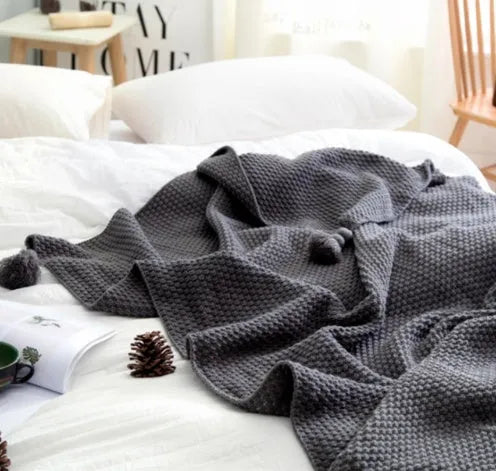 Nordic-style beige acrylic blanket with fringed knit ball detail laid flat.