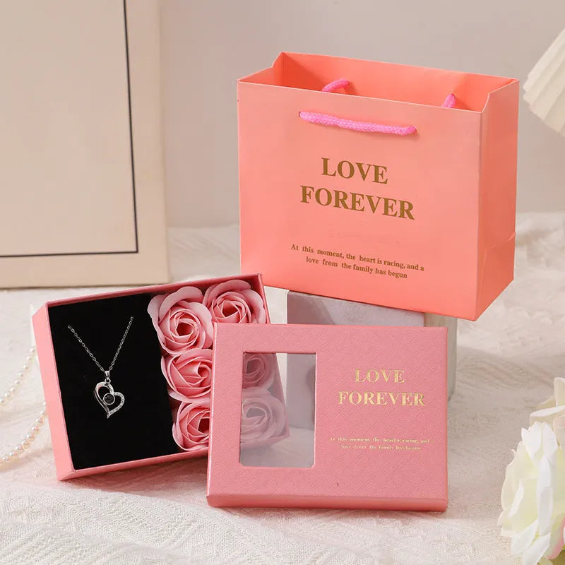 Red, pink, and black soap flower gift sets presented in a box with a handbag-style carrier.