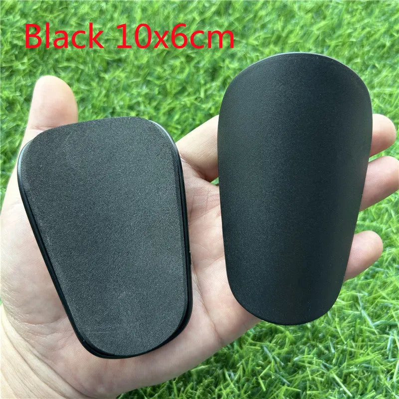 Extra small black and white plastic football shin guards for junior players, size 8cm by 5cm.