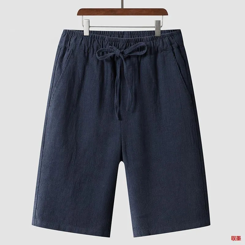 Men's beige linen shorts with loose cropped fit and elasticated waistband laid flat.