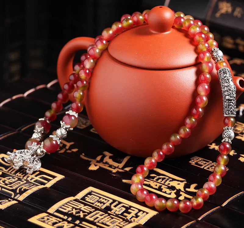 Handmade bracelet with watermelon crystal beads and a red Chinese knot on a white background.
