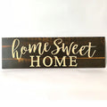 Black wooden wall plaque with carved white HOME SWEET HOME text, showing its rectangular shape.