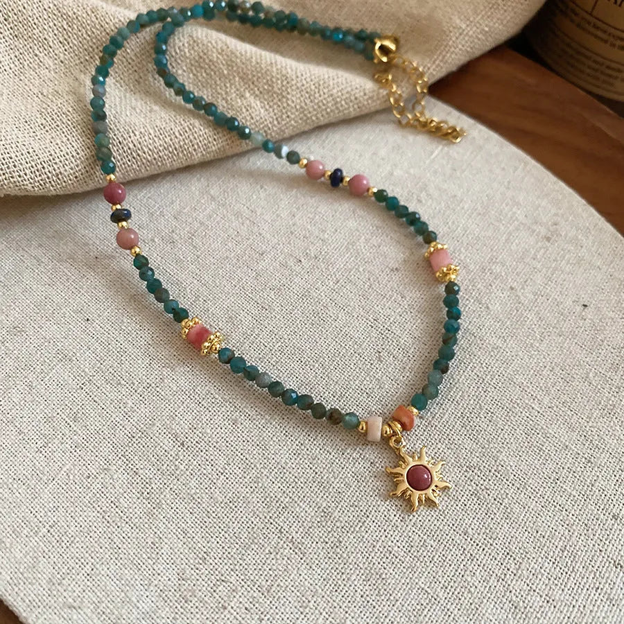 Freshwater pearl necklace with a geometric stone sun pendant on a gold, blue, and pink chain.